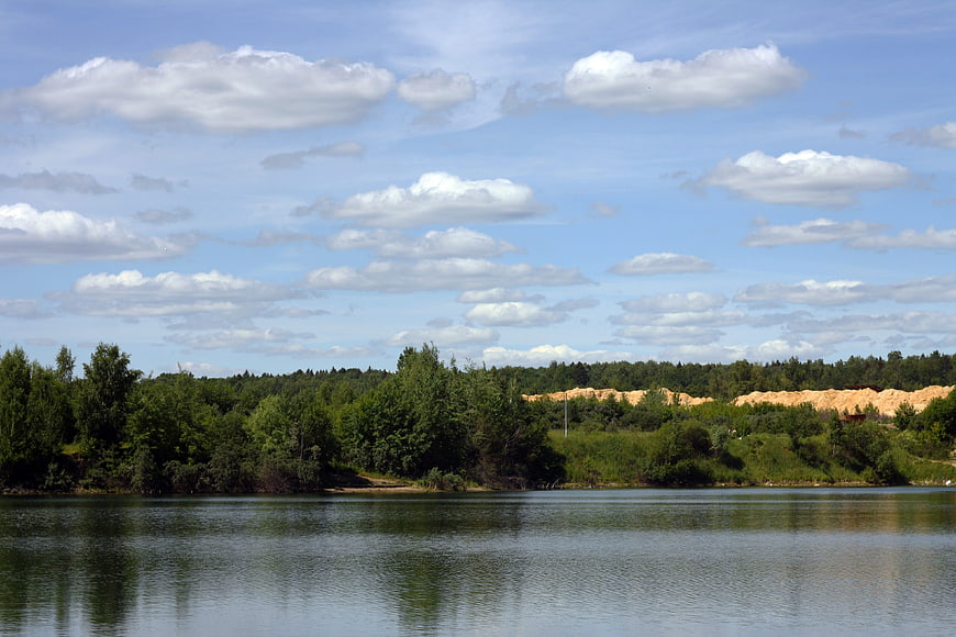 Serene Lake Landscape with Forest and Sandy Hills Under Blue Sky