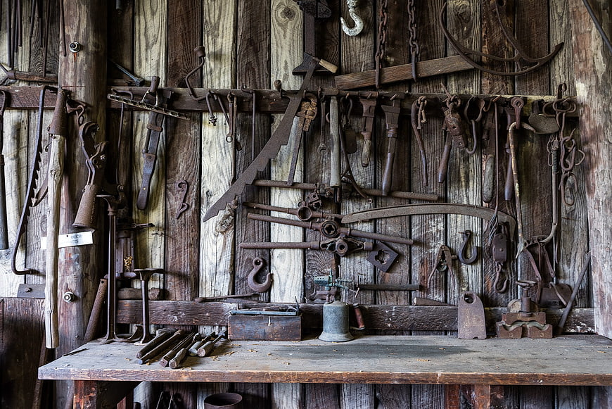 Rusty antique blacksmith tools on rustic wooden workshop wall
