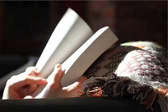 Close-up of hands reading a book under a cozy blanket