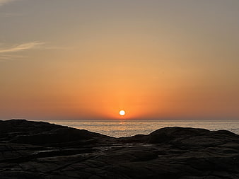 Sunset over rocky coastline with orange sky and calm sea