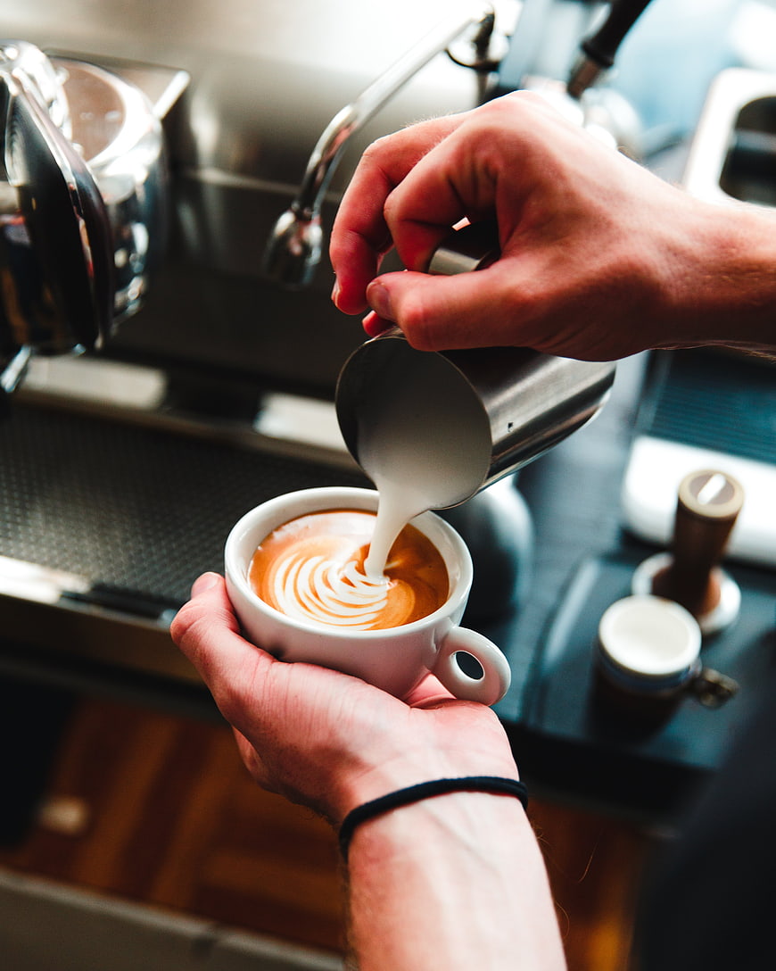 Barista pouring latte art into a white coffee cup
