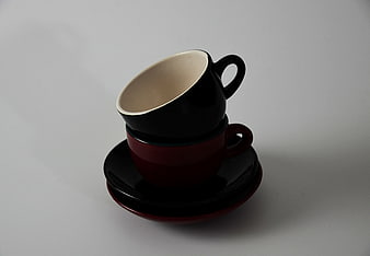 Stacked black and red ceramic coffee cups on saucers
