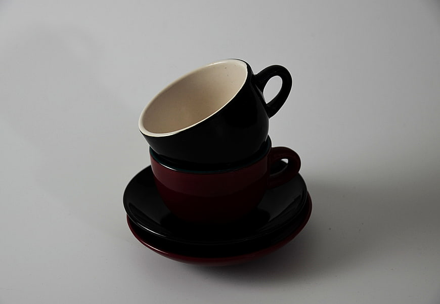 Stacked black and red ceramic coffee cups on saucers
