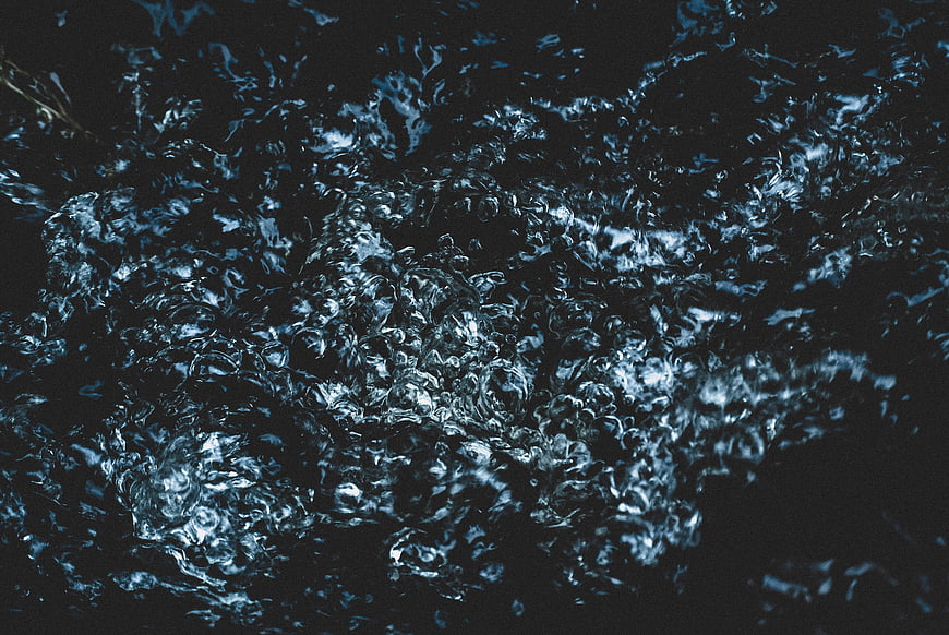Dark turbulent water surface with bubbles and ripples