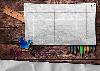 Crumpled graph paper with colored pencils and blue butterfly on wood