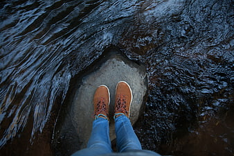 First-person view of brown boots standing on a rock in a river