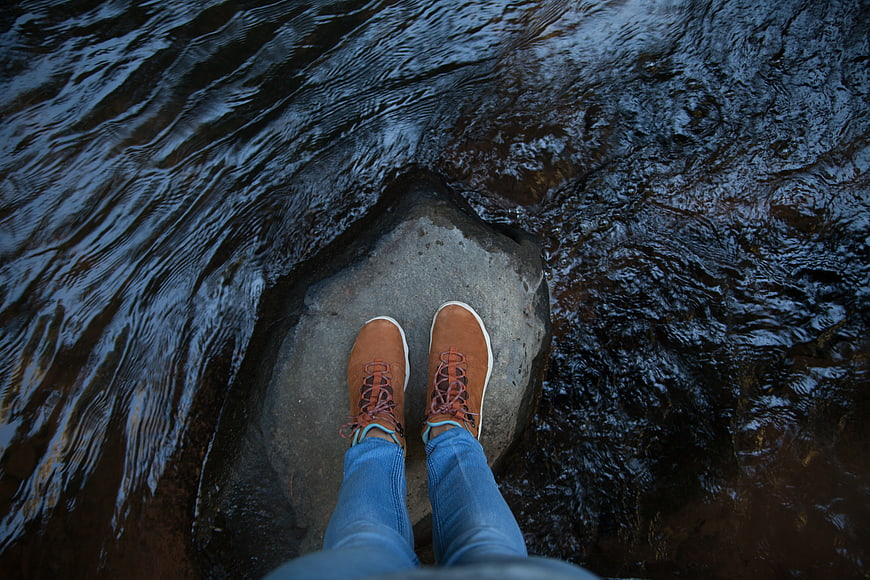 First-person view of brown boots standing on a rock in a river