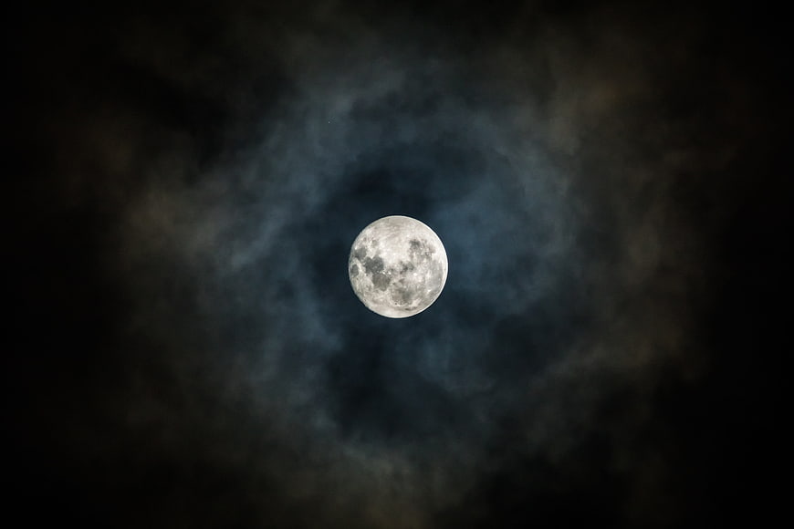 Full Moon Illuminated Through Dark Clouds in Night Sky
