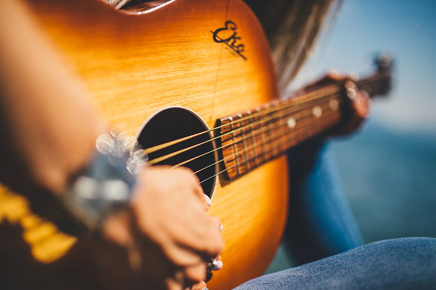 Close-up of hands playing acoustic guitar outdoors