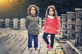 Two young children walking on a stone path in autumn fashion