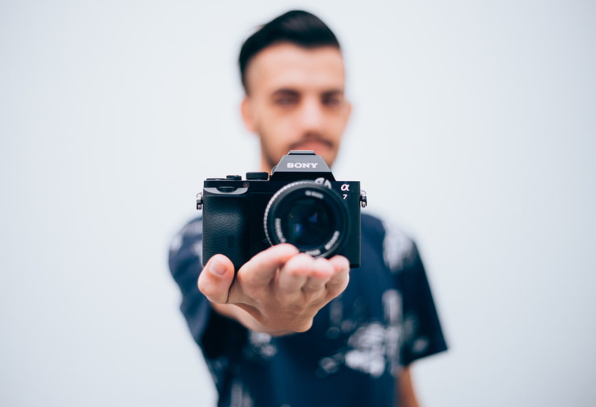 Man holding Sony mirrorless camera towards viewer