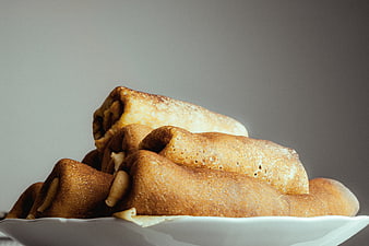 Stack of golden brown rolled crepes on a white plate