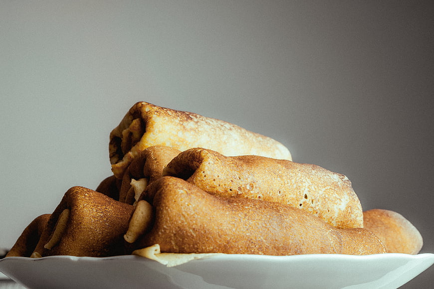 Stack of golden brown rolled crepes on a white plate