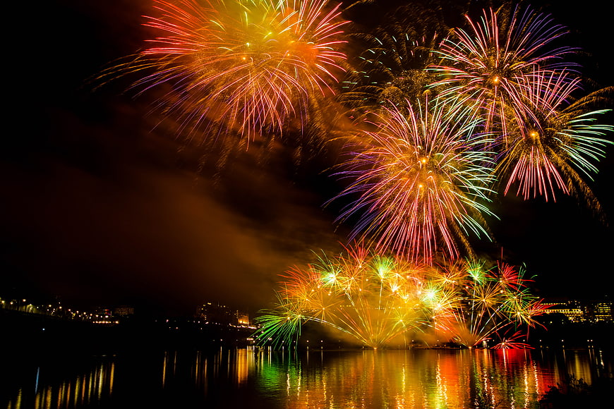 Colorful fireworks exploding over a city river at night