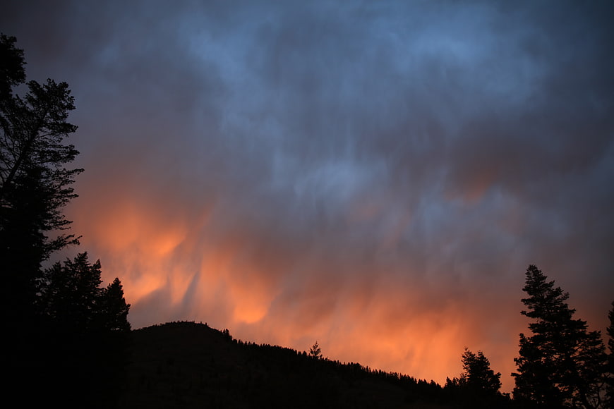 Dramatic wildfire smoke plume over mountain silhouette at dusk