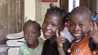 Three smiling children posing together in Haiti