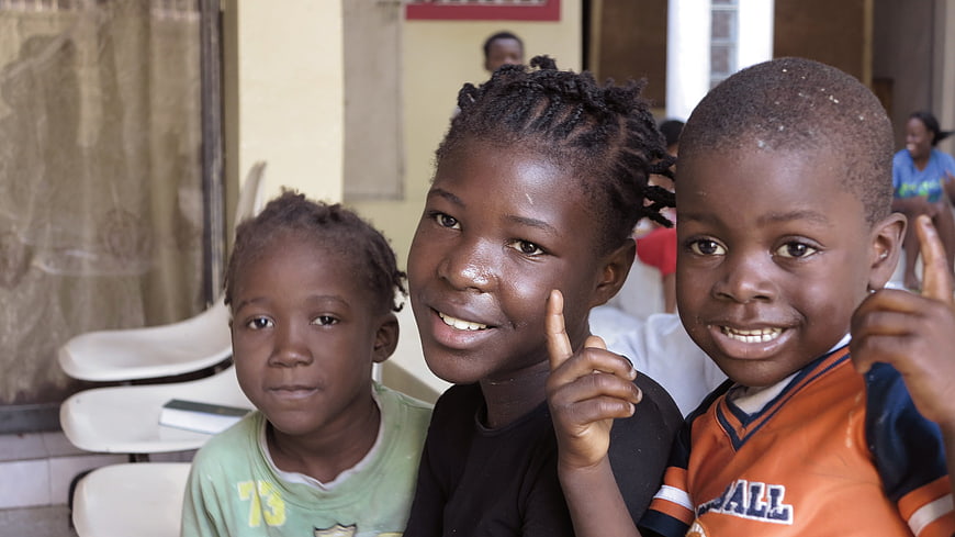 Three smiling children posing together in Haiti