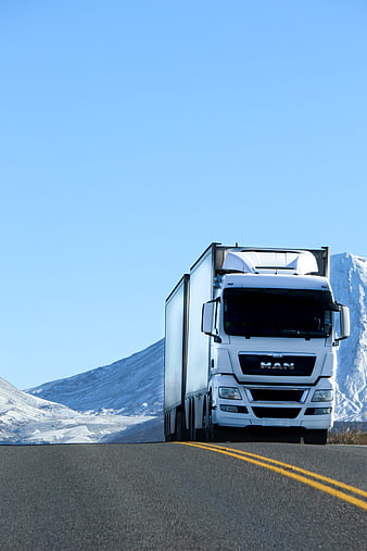 White semi-truck driving on mountain road with snow