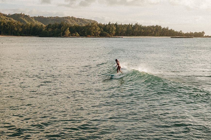 Woman surfing on a wave in tropical ocean with lush hills