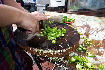 Hands chopping green chili peppers on wooden board