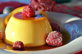 Close-up of creamy caramel flan with frozen raspberries