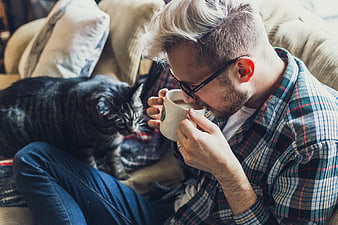 Man drinking coffee with cat on sofa