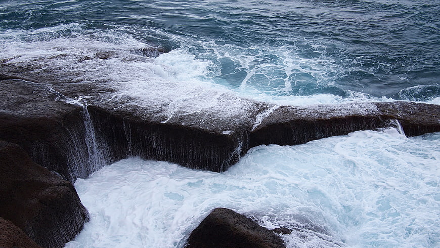 Ocean waves crashing over dark rocky ledge