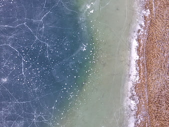 Aerial view of frozen lake ice with cracks and brown grass