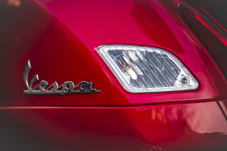 Close-up of red Vespa scooter headlight and logo