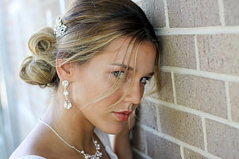 Blonde woman with elegant updo leaning against brick wall