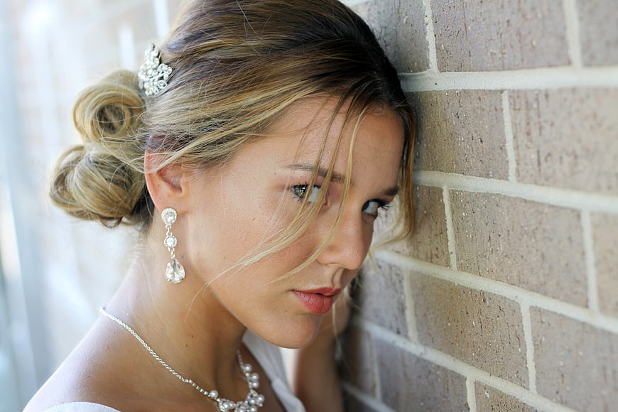 Blonde woman with elegant updo leaning against brick wall