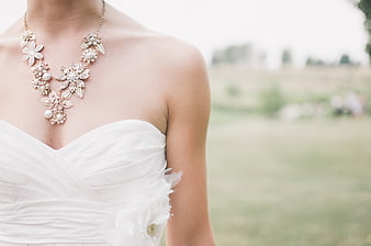 Close-up of bride wearing floral pearl necklace and white dress