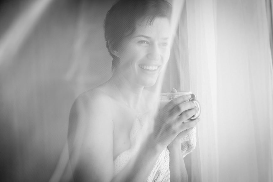 Happy woman drinking coffee through sheer curtain