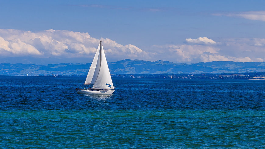 Sailboat Sailing On Lake Constance With Distant Mountains