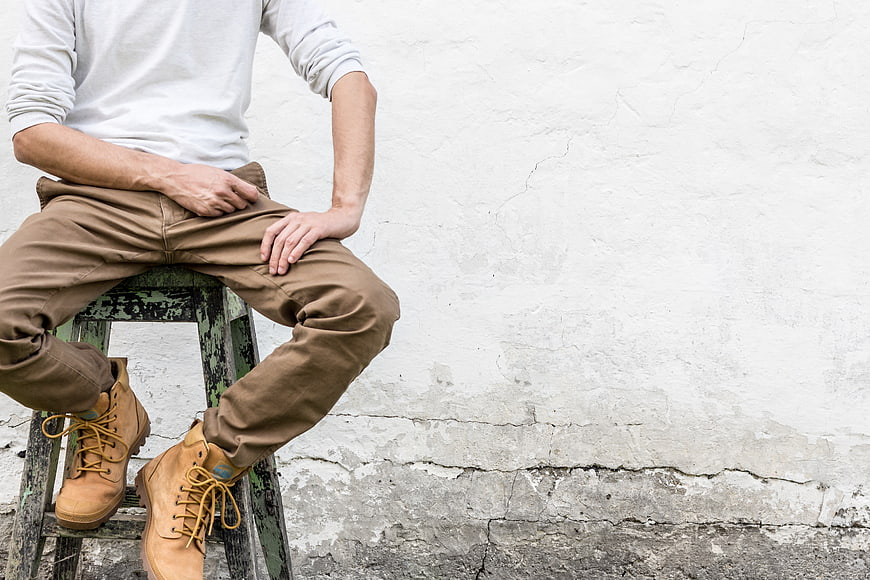 Man in Work Boots Sitting on Stool Against White Wall