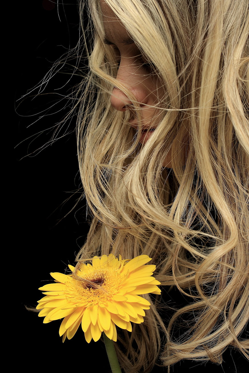 Close-up portrait of blonde woman with yellow gerbera flower