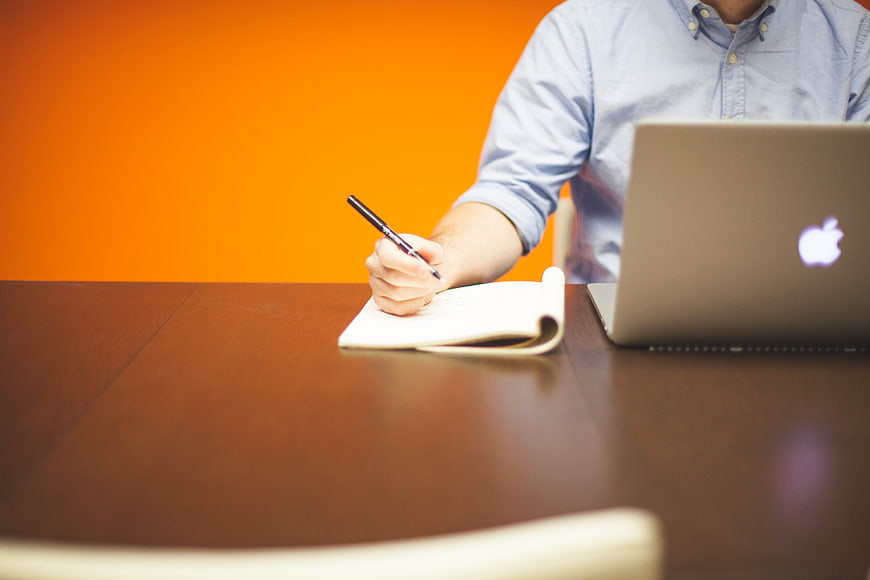 Businessman writing in notebook at desk with laptop