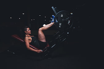 Woman performing leg press exercise in dark gym
