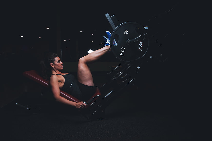 Woman performing leg press exercise in dark gym