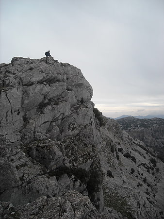 Lone Hiker Sitting on Rocky Mountain Peak Overlooking Valley