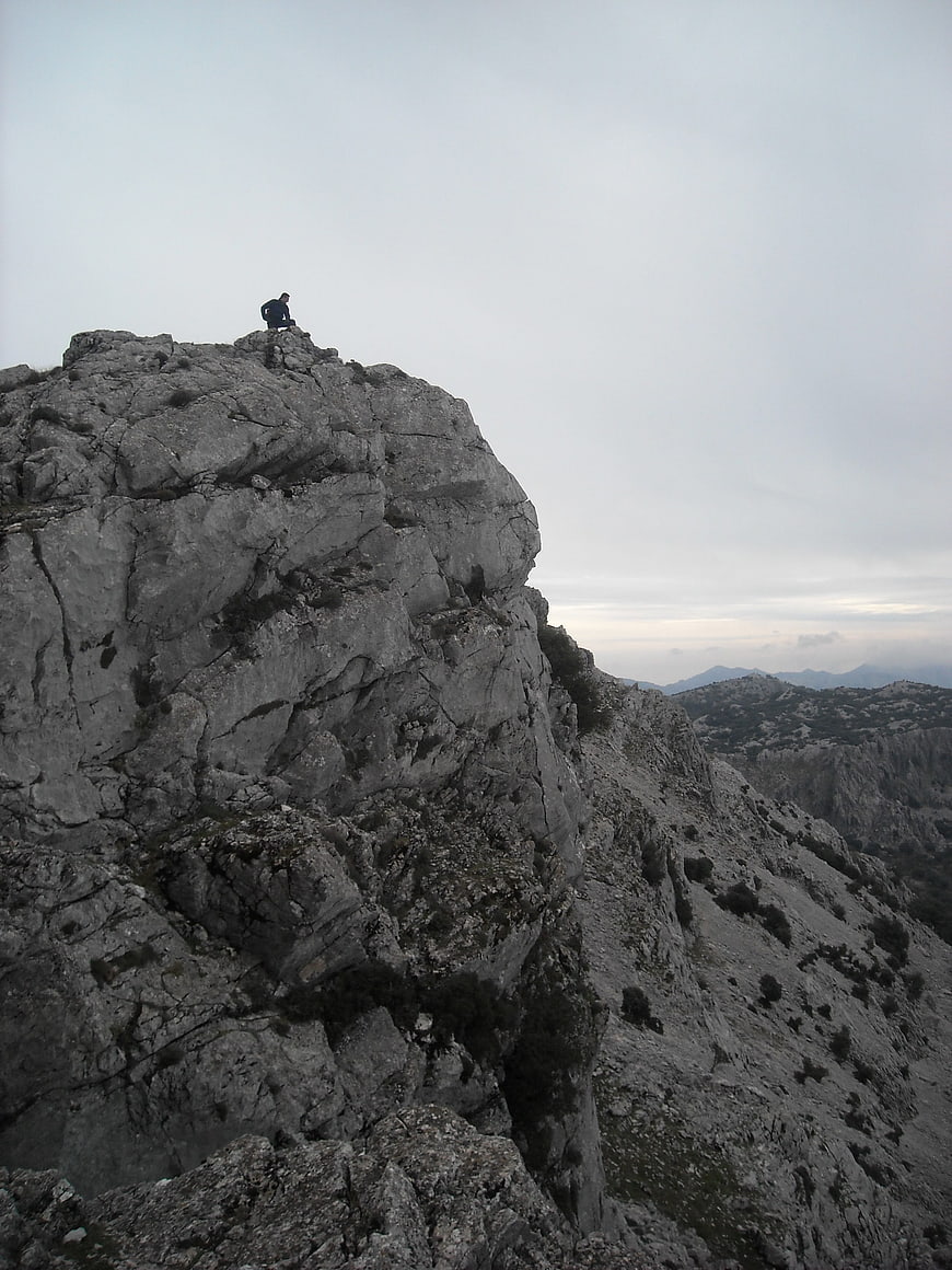 Lone Hiker Sitting on Rocky Mountain Peak Overlooking Valley