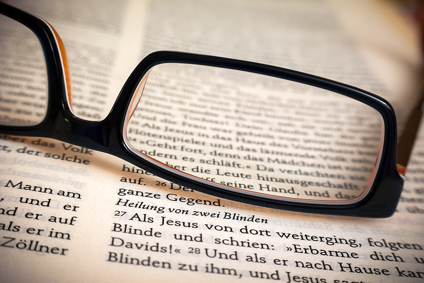 Black reading glasses resting on an open German Bible page