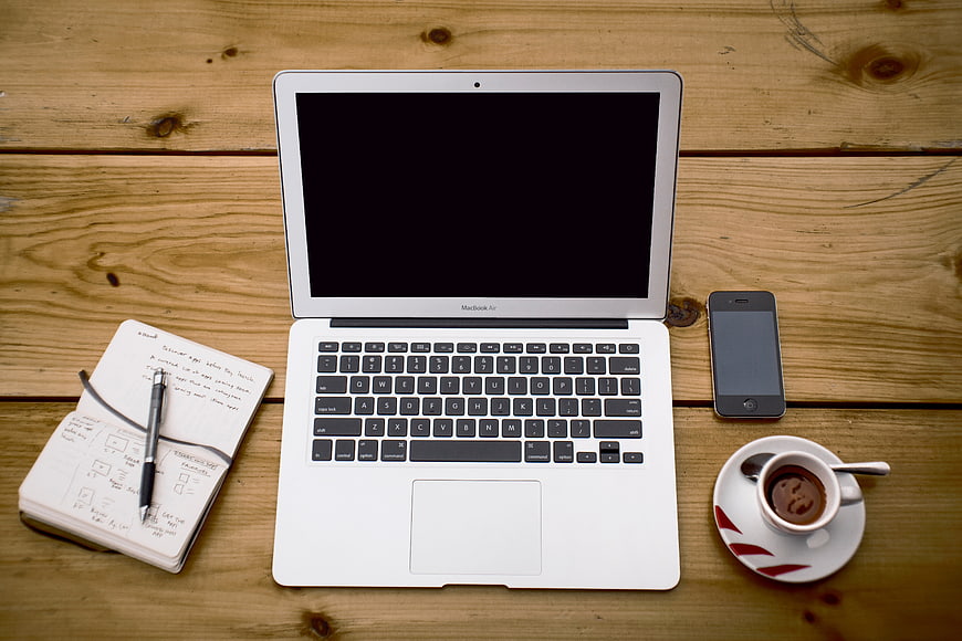 Flat lay of laptop, notebook, coffee, and smartphone on wooden desk