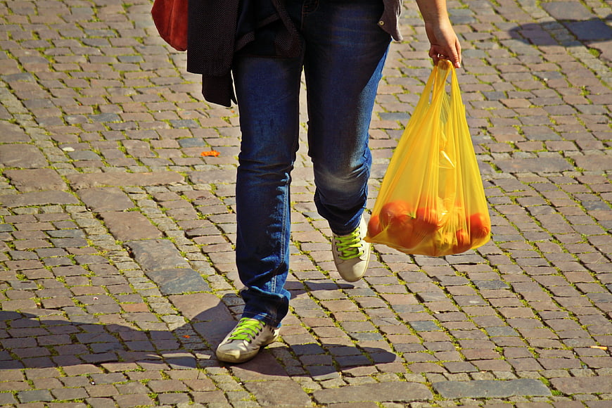 Person walking with yellow plastic bag of oranges on cobblestones