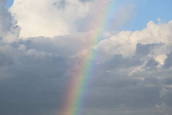 Vertical rainbow beam in cloudy sky with distant airplane