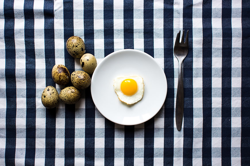 Fried quail egg on plate with raw eggs on checkered tablecloth