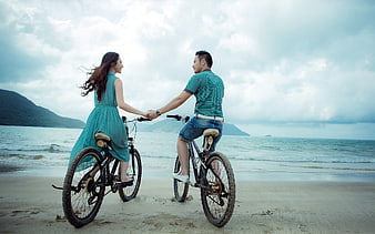 Young Asian couple holding hands on bicycles at the beach