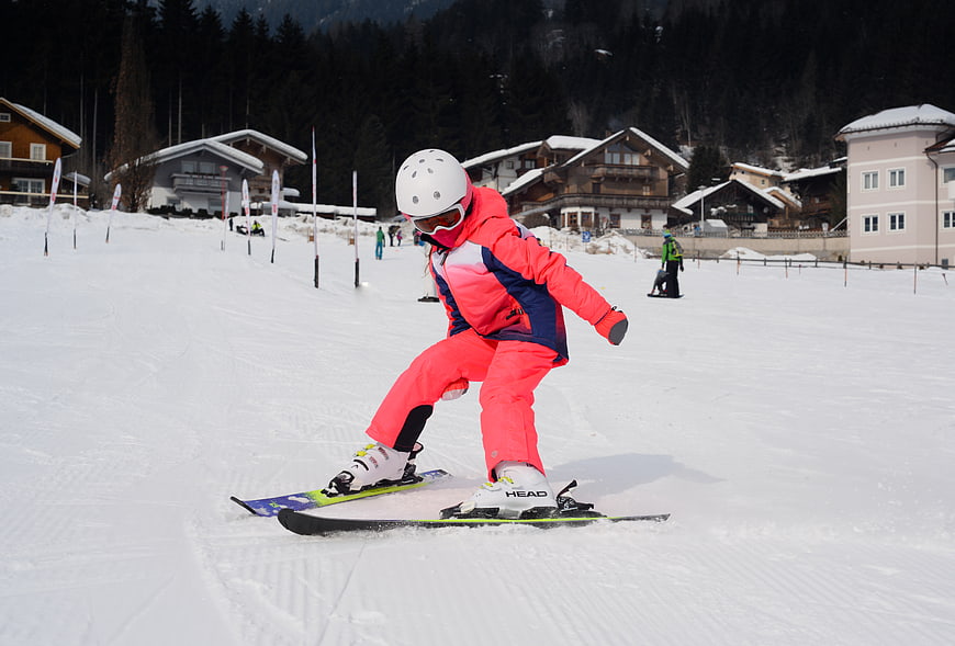 Young girl skiing downhill in bright pink snowsuit