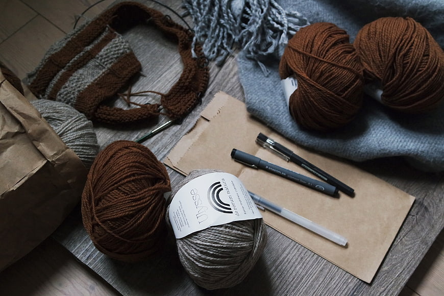 Knitting supplies with yarn, needles, and pens on wooden table