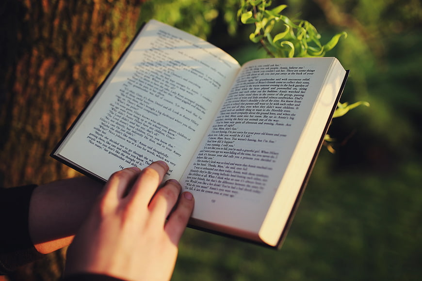 Person reading open book outdoors in sunlight